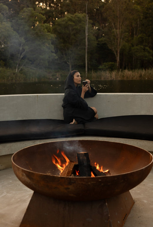 A woman drink a cup of tea by a fire pit