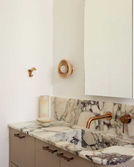 Handmade wooden wall sconce next to a bathroom mirror above a black and white marble bench top.