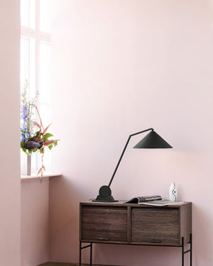 Modern desk with a lamp and open book against a light pink wall.
