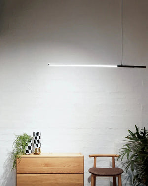 Modern LED linear pendant light hanging above a wooden dresser with a minimalistic interior design.
