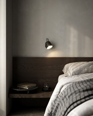 Modern bedroom with a bed, nightstand, and black wall-mounted adjustable light fixture.