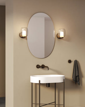Bathroom vanity with oval mirror and wall lights on a beige wall.