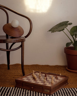 Wooden chessboard with pieces on a rug next to a chair and plant