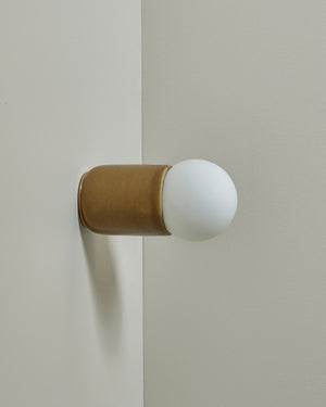 Decorative wall sconce with a gold base and white shade on a neutral background