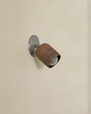 Wall-mounted light fixture with brown shade and metallic base on a beige wall.