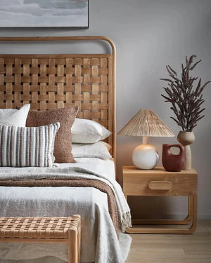 Bedroom with woven headboard, pillows, and a nightstand with a coastal raffia table lamp 