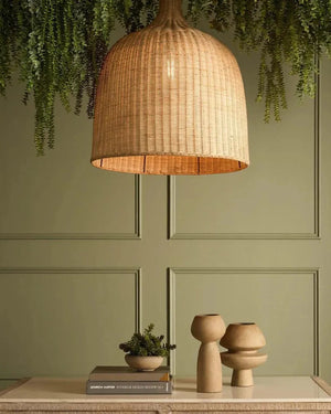 Wicker pendant lamp on a wooden table with decorative items against a green paneled wall.