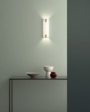 Wall-mounted light fixture on a green wall with a shelf below holding decorative items.