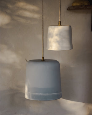 Pendant light with a white shade and blue base hanging against a textured wall.