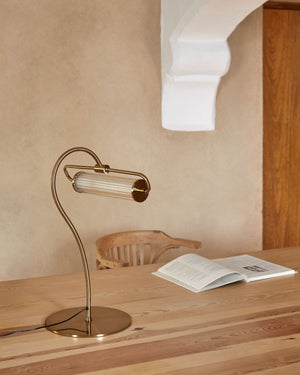 Gold desk lamp on a wooden surface with an open book in the background.
