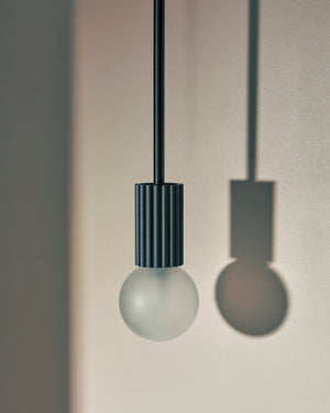 Minimalist pendant light with a black cylindrical shade and white bulb against a neutral background