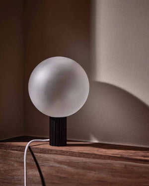 Spherical lamp on a wooden surface with a soft shadow on a neutral wall.
