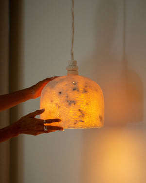 Hand holding a textured pendant light with warm glow against a blurred background