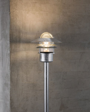Scandinavian Style Bollard Light in Galvanised Steel Finish against a concrete wall - Lighting Collective 