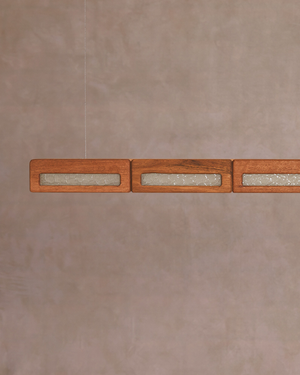 Mid-Century linear pendant light with rectangular wood-grain shades containing textured clear glass panes, suspended against a warm wall