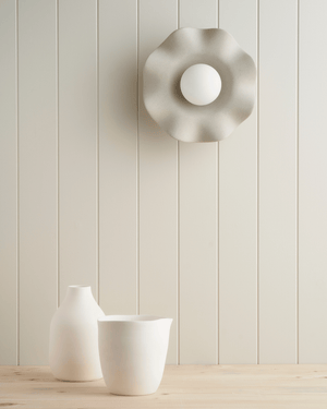frill wall sconce on light grey background with pottery underneath

