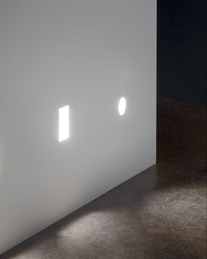 Two square light fixtures on a white wall casting shadows on a dark floor.