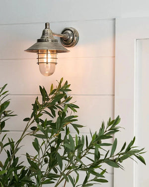 Vintage-style wall light fixture on a white wall with a plant in the foreground.