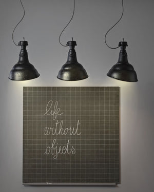 Three industrial-style pendant lights above a framed artwork with text on a gray wall.