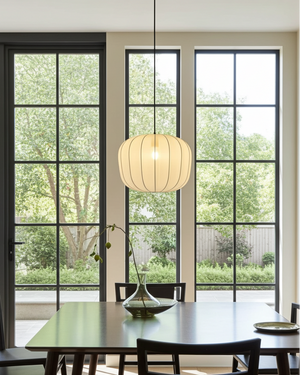 Dining room with large windows, a hanging ivory chiffon light fixture, and a table. 