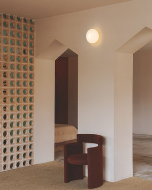 Modern interior with a brown chair against a textured wall and an frosted orb wall light