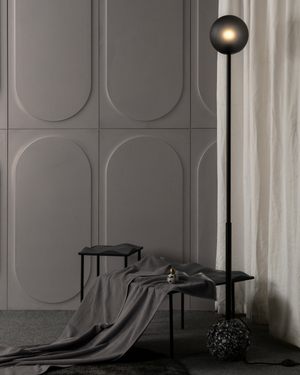 Modern interior with a floor lamp, bench, and draped fabric against a textured wall.