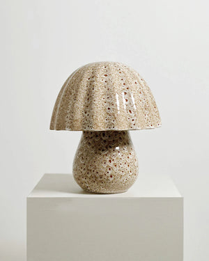 Ceramic table lamp with textured design on a white pedestal against a light gray background