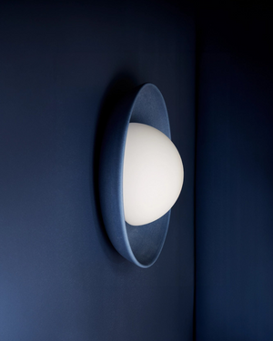 Wall-mounted light fixture in dark blue with a white bulb on a dark blue wall