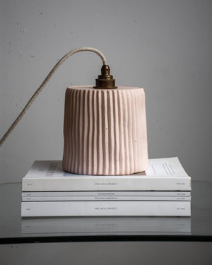 Concrete pendant light with pleated design on top of books