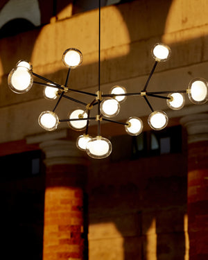 Modern chandelier with multiple light bulbs hanging in a room with brick walls.
