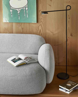 Gray armchair with an open book, black floor lamp, and books on a wooden floor.