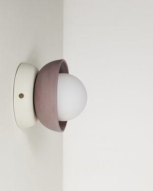 Wall-mounted light fixture with a white bulb and pinkish-brown cover on a plain wall.
