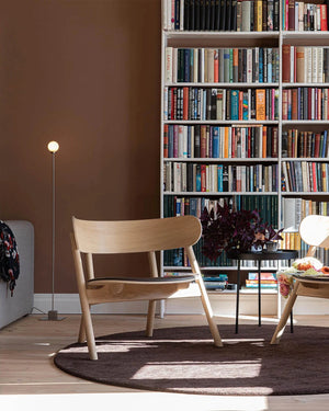 Modern living room with wooden chairs, a round rug, and a bookshelf filled with books.