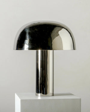 Chrome table lamp on a white pedestal against a light gray background