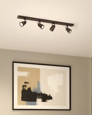 Minimalist four spotlight bronze bar fixture on white ceiling above abstract painting