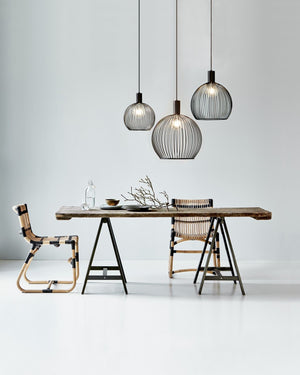 Modern dining area with a wooden table, chairs, and black cage-like pendant lights against a white wall.