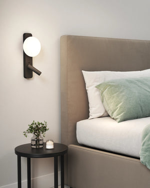 Bedroom with a bed featuring green and white bedding, a nightstand with a plant and candle, and wall sconce.