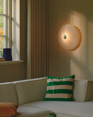 Living room with a beige sofa, green and white striped pillow, and a wall-mounted pleated light.