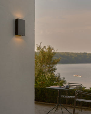 Outdoor wall light fixture on a white wall with a scenic view of trees and water.