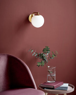 Modern wall light fixture on a red wall with a pink armchair and small table with a vase and books.