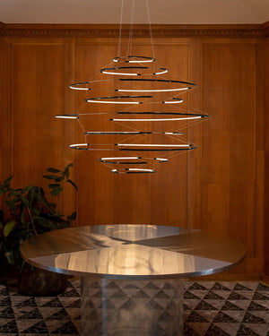 Black Modern chandelier hanging above a round table in a room with wooden walls and patterned floor.