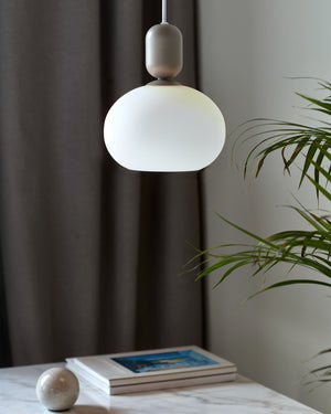 Grey Modern pendant light hanging above a table with books and a plant in a minimalistic setting.