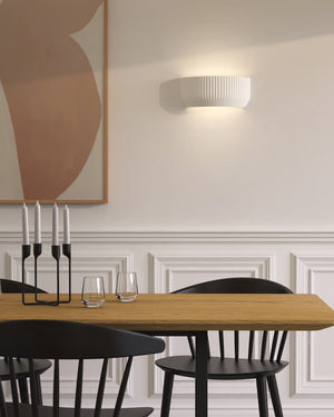 Dining room with wooden table and black chairs against a wall with abstract art and a pleated plaster light fixture.