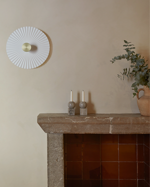 Decorative wall light fixture above a stone fireplace with candles and a plant.