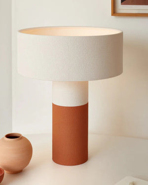Table lamp with a textured white shade and terracotta base on a light surface.