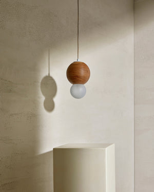 Pendant light with wooden shade and white bulb hanging against a neutral wall.