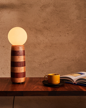 Timber Stripy Table Lamp | Buddy on a wooden table next to a cup and book against a brown background Vic Ash and Redgum