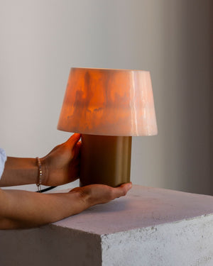 Person holding a small lamp with a warm glow on a concrete surface.