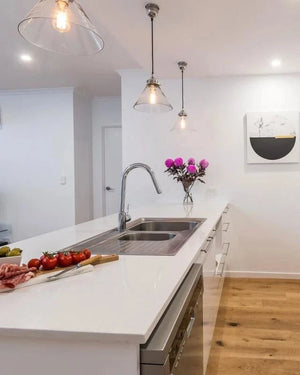 Modern kitchen with white countertops, stainless steel sink, and vintage glass pendants