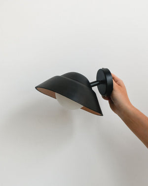 Hand holding black leather wall light with adjustable arm against beige background